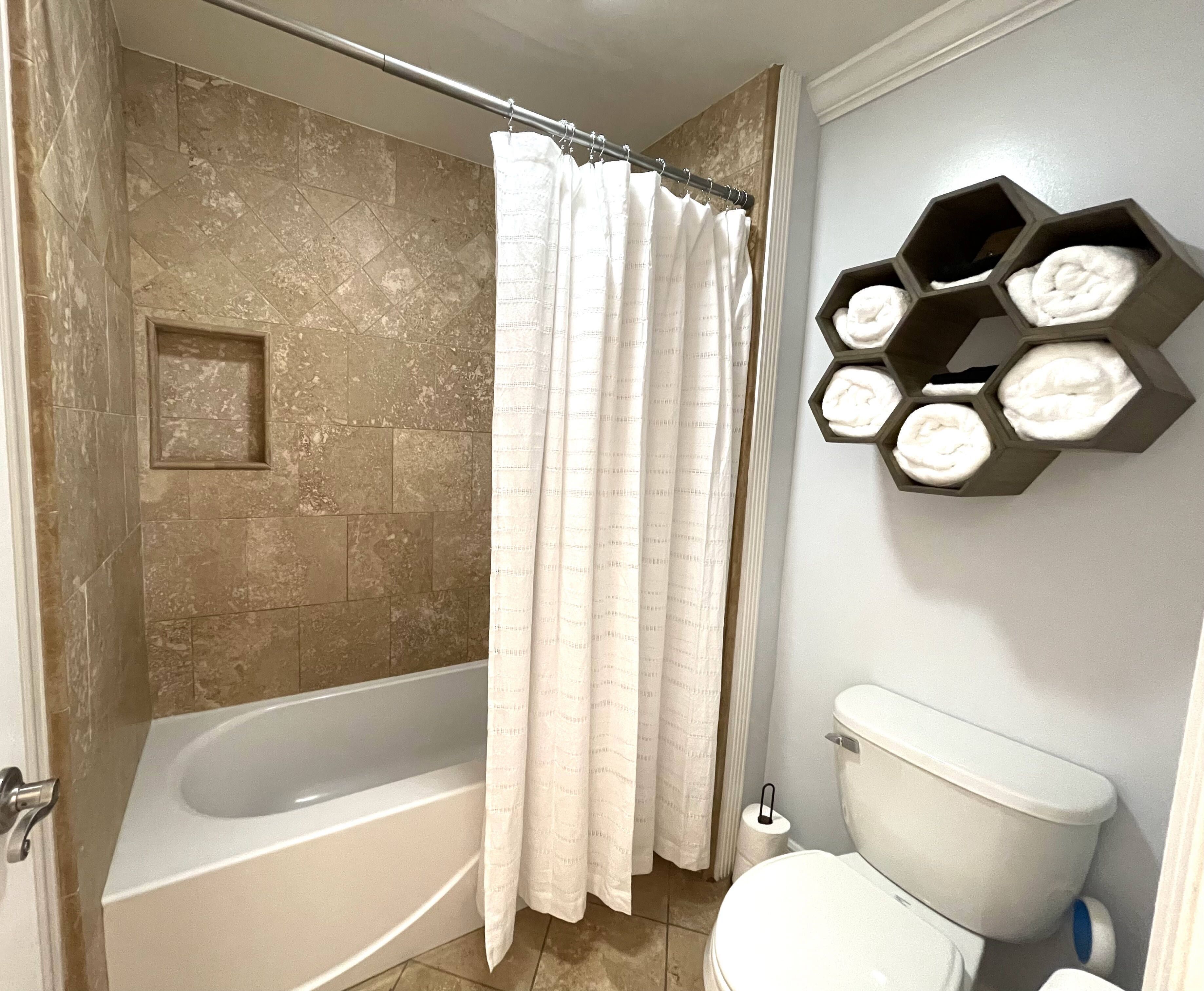 A bathroom with a bathtub, a toilet, and a shower curtain. There are hexagonal shelves with towels on the wall.