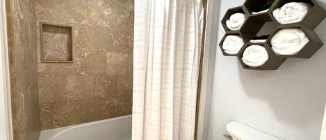 A bathroom with a bathtub, a toilet, and a shower curtain. There are hexagonal shelves with towels on the wall.