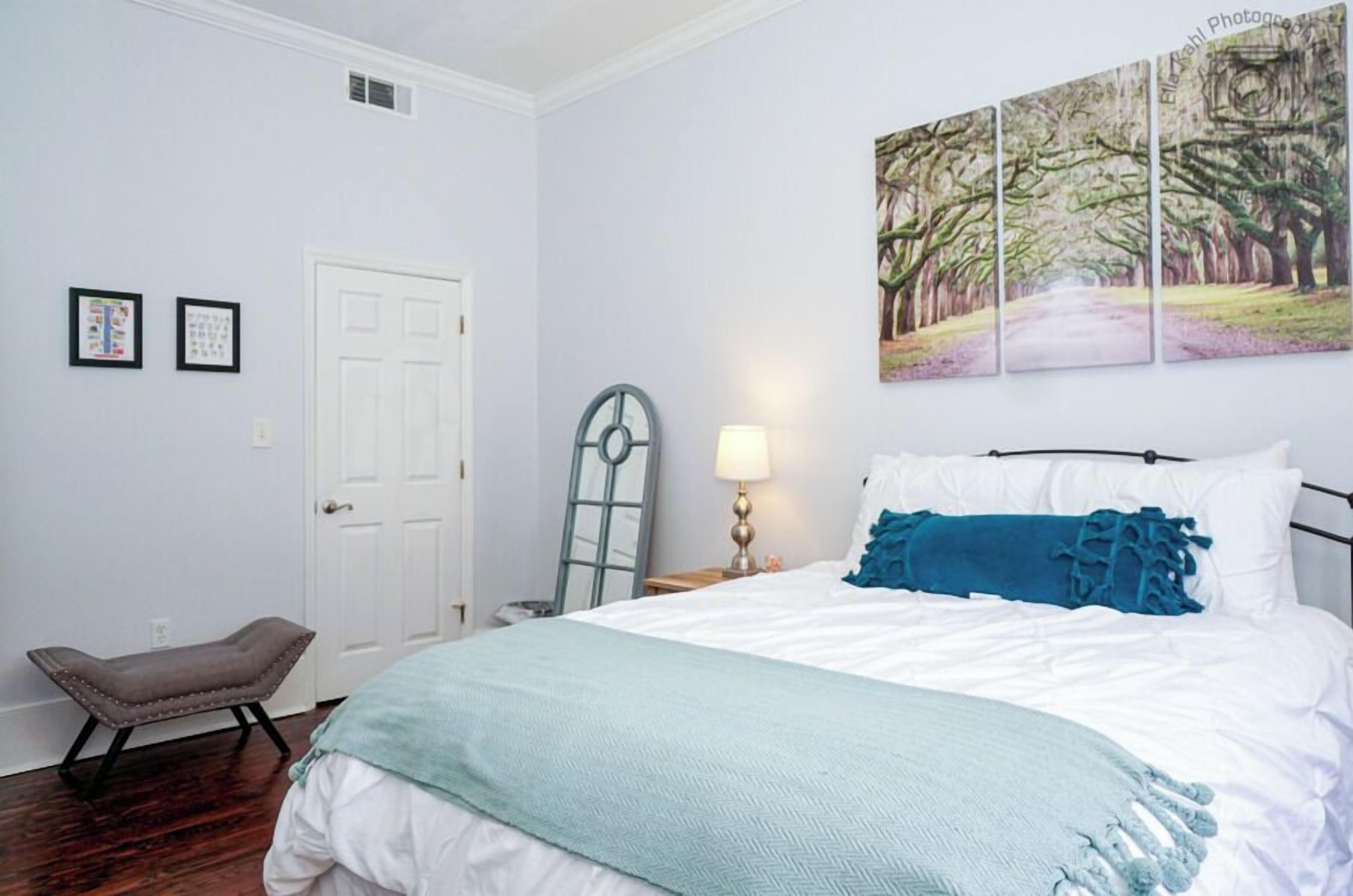 A bedroom with a bed, a nightstand, a lamp, a bench, and a door.