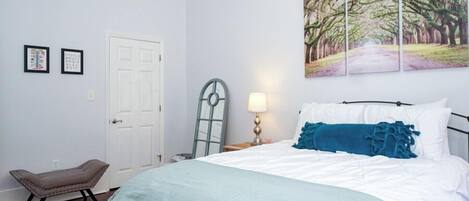 A bedroom with a bed, a nightstand, a lamp, a bench, and a door.
