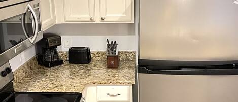 Una cocina con armarios blancos, un refrigerador de acero inoxidable, un microondas, un tostador y una cafetera.