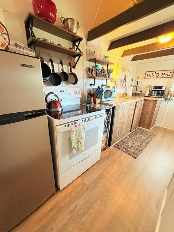 A kitchen with a white refrigerator, a red kettle, and a microwave. There are wooden cabinets and a rug on the floor. - Cozy Cottage 1bed 1bath in Slocomb Al (Slocomb)