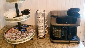 A kitchen counter with a coffee maker, a tiered tray of snacks, a mug with travel-themed writing, and a sign saying "let's eat". - Cozy Cottage 1bed 1bath in Slocomb Al (Slocomb)