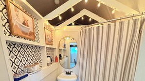 A compact bathroom with a white sink, a mirror, and a toilet. There are decorative lights on the ceiling, a black rug on the floor, and a striped shower curtain. - Cozy Cottage 1bed 1bath in Slocomb Al (Slocomb)