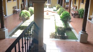 A courtyard with a stone archway, tiled flooring, and a view of a garden with neatly trimmed bushes and a fountain. - La mansión  (San Isidro)