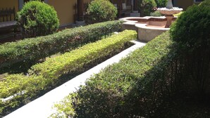 A courtyard with a fountain, neatly trimmed hedges, and a building with yellow walls and a tiled roof. - La mansión  (San Isidro)