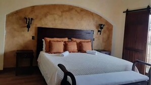 A bedroom with a large bed, a wooden headboard, two bedside tables, and a wooden door. - La mansión  (San Isidro)