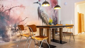 Un espace repas agrémenté d’une fresque murale, de chaises en bois, d’une table, de luminaires suspendus et d’un radiateur.