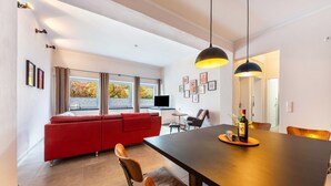 Un salon moderne avec un canapé rouge, une table à manger et des chaises, un téléviseur et des tableaux encadrés accrochés au mur.