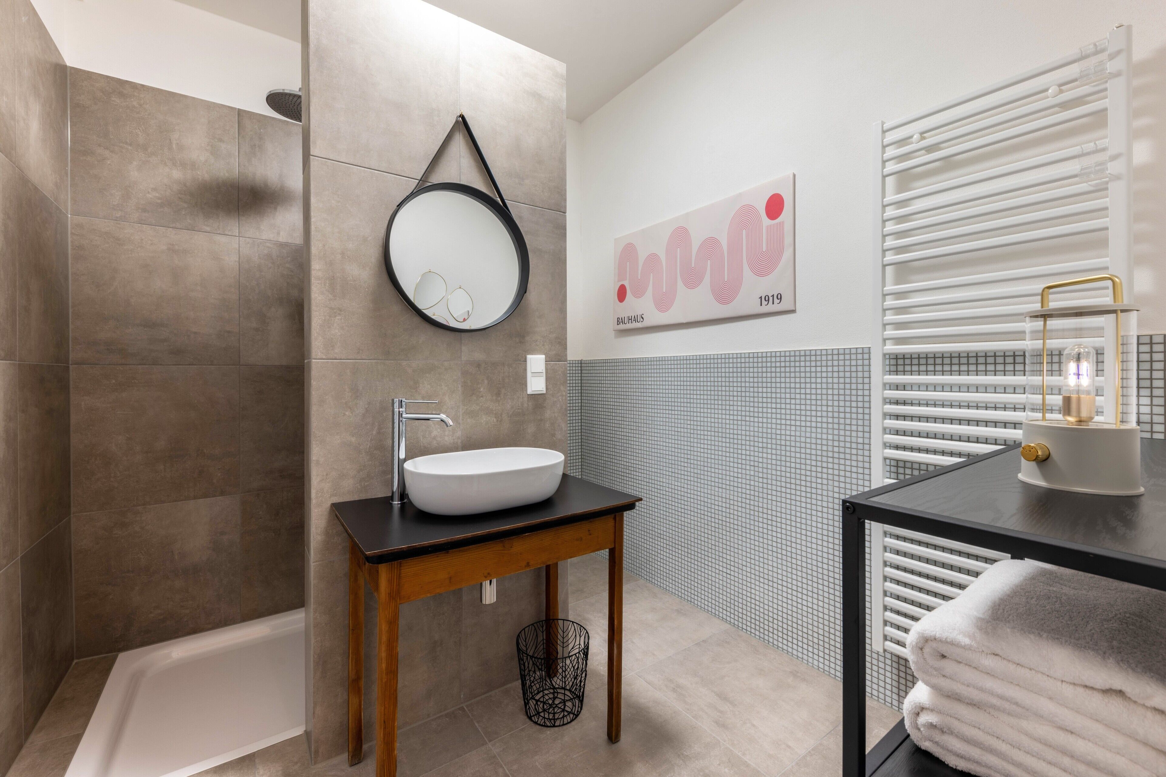 Une salle de bain moderne avec un lavabo sur pied, un miroir rond, un porte-serviettes et un radiateur.