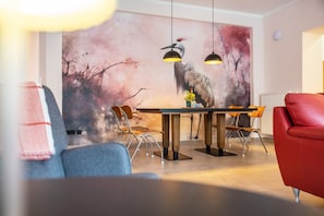 A dining area with a mural, wooden table, and modern chairs. - Suites at the Historic Berghotel Johanna (Eslohe (Sauerland))