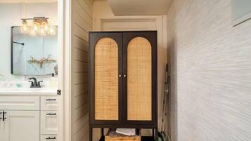 Un baño con tocador, espejo, armario con puertas de mimbre y toallero de pared.