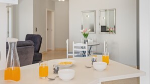 Ein moderner Essbereich mit einem weißen Tisch, gedeckt für das Frühstück, inklusive Schüsseln, Gläsern und einer Kanne Orangensaft.