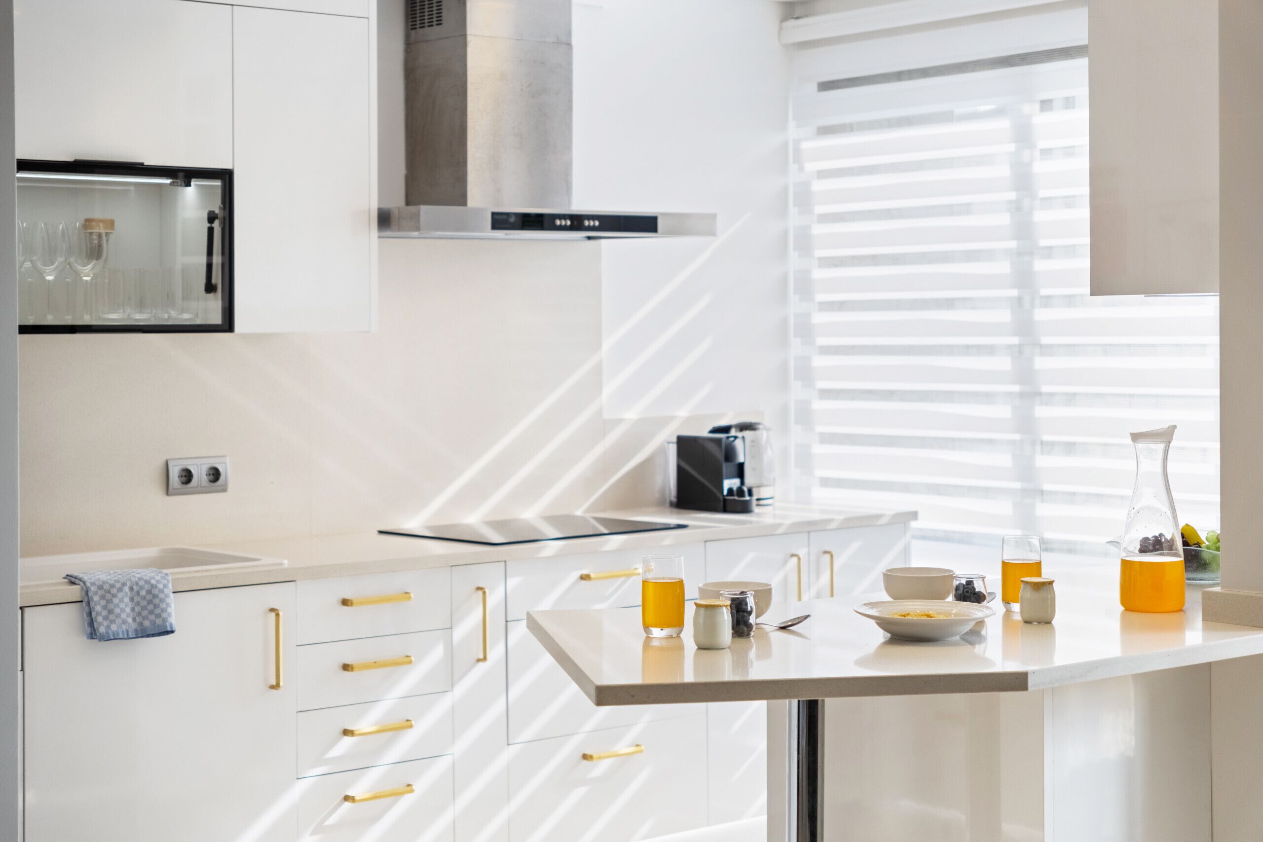 A modern kitchen with white cabinets, a stainless steel range hood, and a breakfast bar.