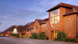 A row of brick buildings with large windows and a parking lot in front. - Dale Hill Hotel (Ticehurst)