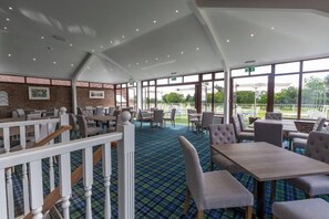 A spacious indoor area with tables and chairs, large windows, and a view of the outdoors. - Dale Hill Hotel (Ticehurst)