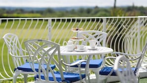 A white metal outdoor seating area with blue cushions, a small round table with a teapot, cups, and a sandwich. - Dale Hill Hotel (Ticehurst)