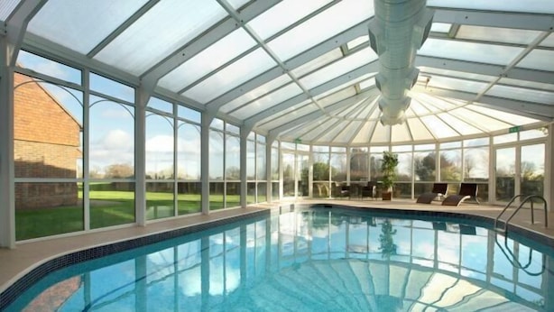 A covered swimming pool with a glass roof, surrounded by a brick wall and a grassy area. - Dale Hill Hotel (Ticehurst)