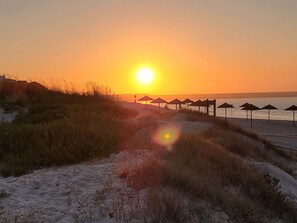Uma praia com um pôr do sol, dunas de areia e guarda-sóis.