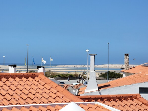 Vista costeira com telhados em terracota, céu claro e bandeiras hasteadas.