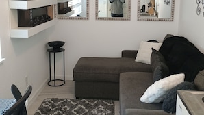 A living room with a gray sofa, a patterned rug, and a flat-screen TV on a white shelf. - Lovely studio in Sacramento near downtown. (Sacramento)