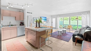 A modern kitchen with a central island, a dining area with a table and chairs, and a living room with a sofa and a coffee table.