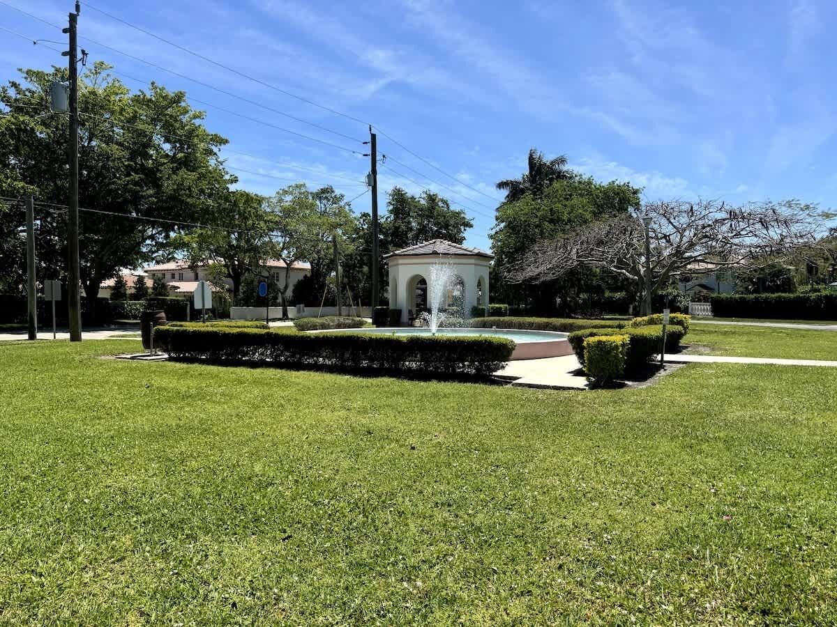 Un jardí ben cuidat amb una font, envoltat d'arbres i arbustos podats i un edifici petit amb teulada circular.