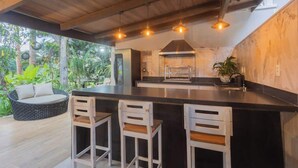 A modern kitchen with a large island, bar stools, and a view of lush greenery.