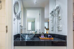 A bathroom with a glass bowl sink, two wall-mounted mirrors, a hairdryer, and a small potted plant. - Charming Apartment with Pool in Botafogo (Rio de Janeiro)