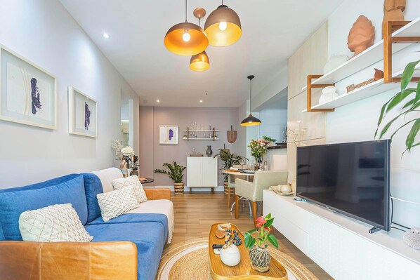 A modern living room with a blue sofa, a wooden coffee table, and a flat-screen TV. - Charming Apartment with Pool in Botafogo (Rio de Janeiro)