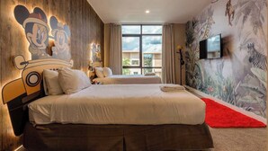Une chambre d’hôtel avec deux lits, une grande fenêtre, une fresque murale représentant des personnages de dessins animés et un téléviseur fixé au mur.