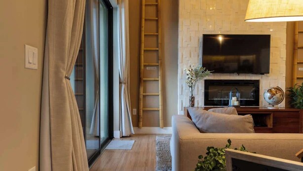 Un salon moderne doté d’un téléviseur à écran plat fixé au-dessus d’une cheminée, d’un canapé avec des coussins et d’une porte-fenêtre coulissante donnant sur un balcon.