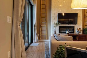 Un salon moderne doté d’un téléviseur à écran plat fixé au-dessus d’une cheminée, d’un canapé avec des coussins et d’une porte-fenêtre coulissante donnant sur un balcon.
