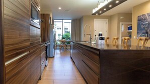Une cuisine moderne avec un lambris en bois, un îlot central doté de chaises et une vue sur l’extérieur.