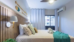 Ein Schlafzimmer mit einem Bett, Kissen, einer Nachttischlampe, einem Fenster mit Vorhängen und einer Klimaanlage.