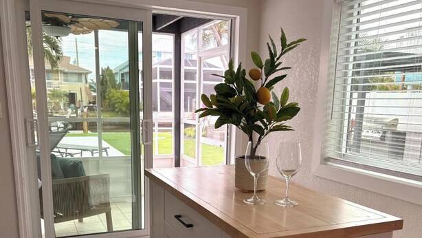 Eine Küche mit Holzarbeitsplatte, weißen Schränken, einer Glastür und einem Blumentopf mit Vase und Weingläsern.