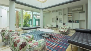 Een ruime woonkamer met een grote ronde tafel, bloemensofa's en een kamerkleed met dessin.