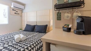 Een hotelkamer met een bed, een koffiezetapparaat, een plank met keukengerei, en een bord aan de muur.