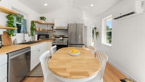 Une cuisine moderne avec des meubles blancs, des appareils en acier inoxydable et une table à manger en bois, accompagnée de chaises.