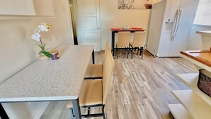 A compact kitchen with a dining table, chairs, a refrigerator, and a painting on the wall.