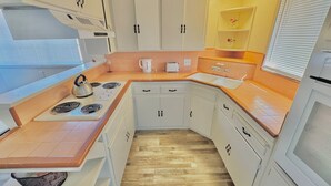 A compact kitchen with white cabinets, a gas stove, a kettle, and a sink.