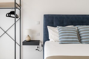 A neatly arranged hotel room with a bed, a bedside lamp, a shelf with a lamp, and a wall-mounted rack with hangers.