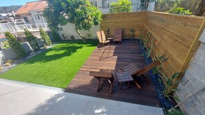 A wooden deck with outdoor furniture, a grassy lawn, and a garden wall.