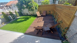 Una terraza de madera con mobiliario exterior, césped y un muro de jardín.