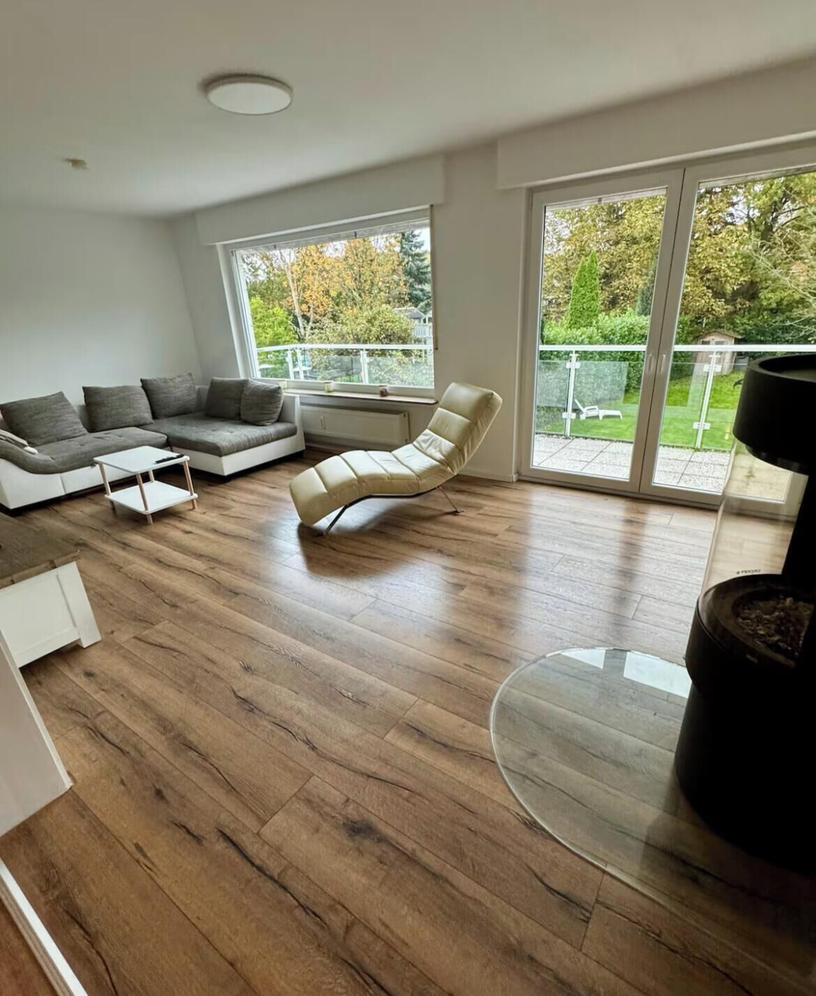 A modern living room with a wooden floor, a grey sofa, a beige armchair, and a glass coffee table.