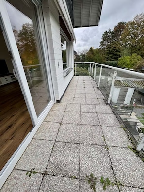 Um edifício moderno com área externa coberta, piso de azulejos e guarda-corpos de vidro.