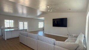 A spacious living area with a large sectional sofa, a flat-screen TV mounted on the wall, and a ceiling fan. - Newly Remodeled Chandler Gem — Stylish 3 Bed, 2 Bath Home Awaits! (Chandler)