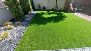 Une pelouse bien entretenue, avec un chemin de gravier, entourée de différentes plantes et agrémentée d’une terrasse en bois.