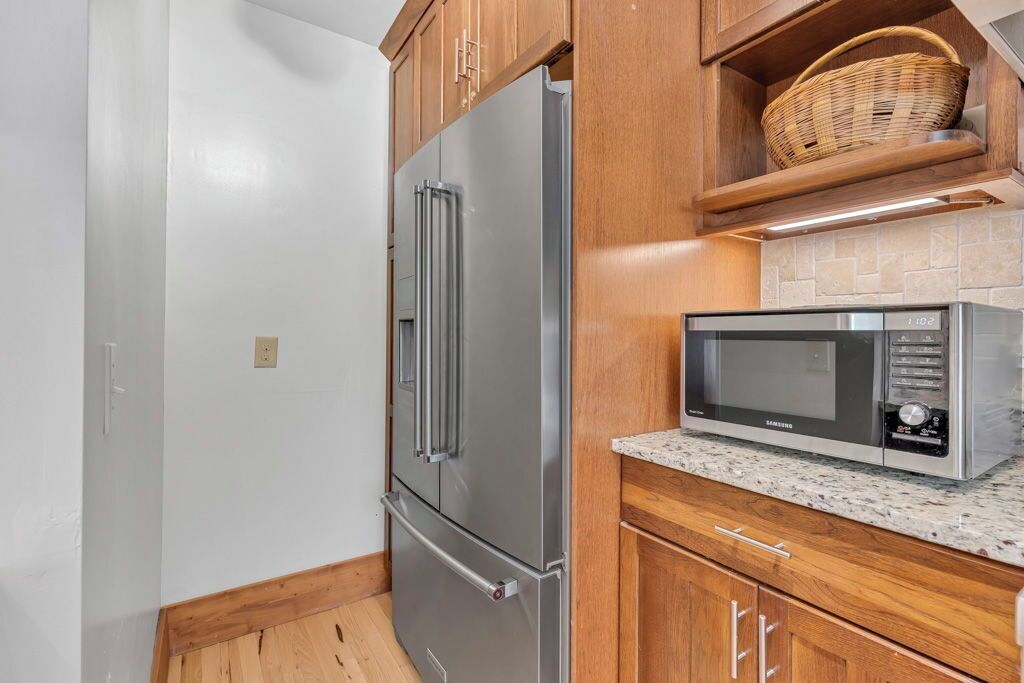 A kitchen with a stainless steel refrigerator, a microwave, wooden cabinets, and a granite countertop.