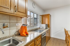 Een keuken met houten kastjes, een roestvrijstalen spoelbak, een magnetron en een raam met uitzicht.